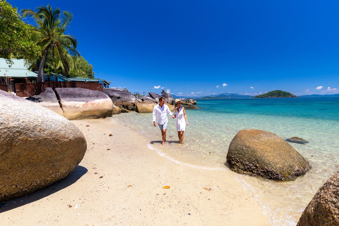 Two guests walking along the white sand beach between granite boulders